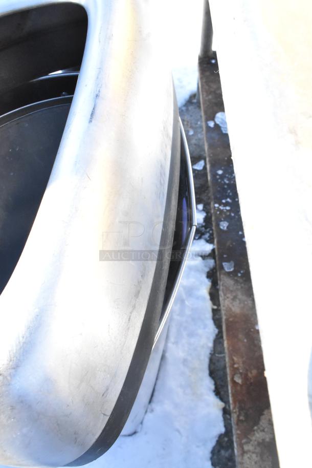 SimpleHuman metal trash can with contents, showing a sleek design and brushed finish, on snow and concrete background.