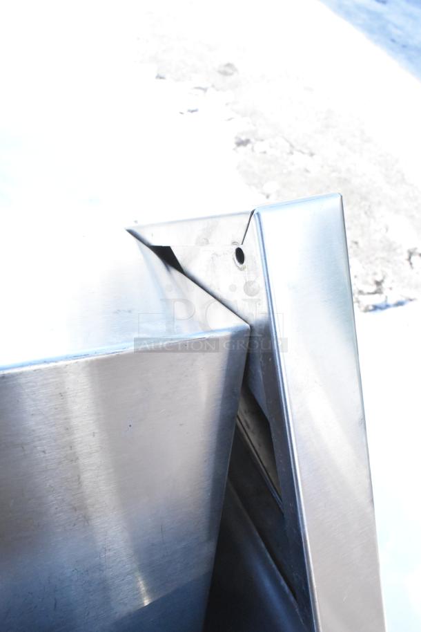 Stainless steel trash can shell with a swinging flap lid, showing brushed metal finish and minor surface wear.