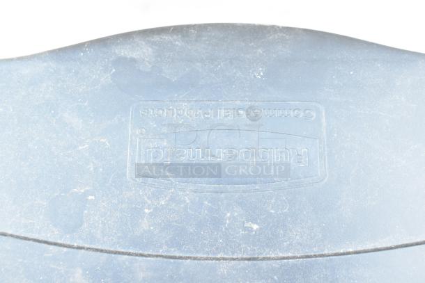 Rubbermaid poly trash can lid, commercial grade, shows some wear. Logo embossed on surface. Suitable for heavy-duty use.