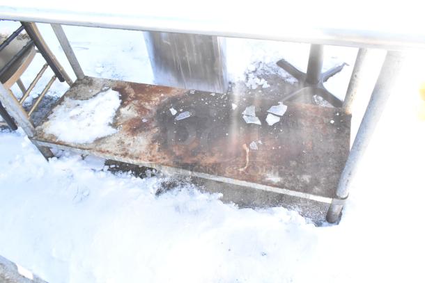 Stainless steel table with metal under shelf, commercial can opener mount, weathered condition, some rust and snow.