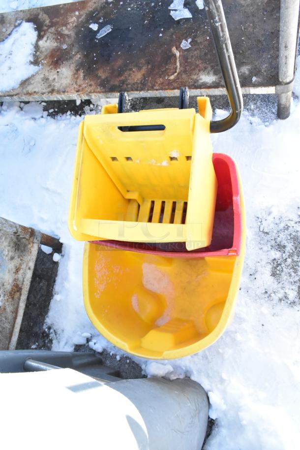 Rubbermaid yellow poly mop bucket with wringing attachment, visible wear, on commercial casters. Snowy outdoor setting.