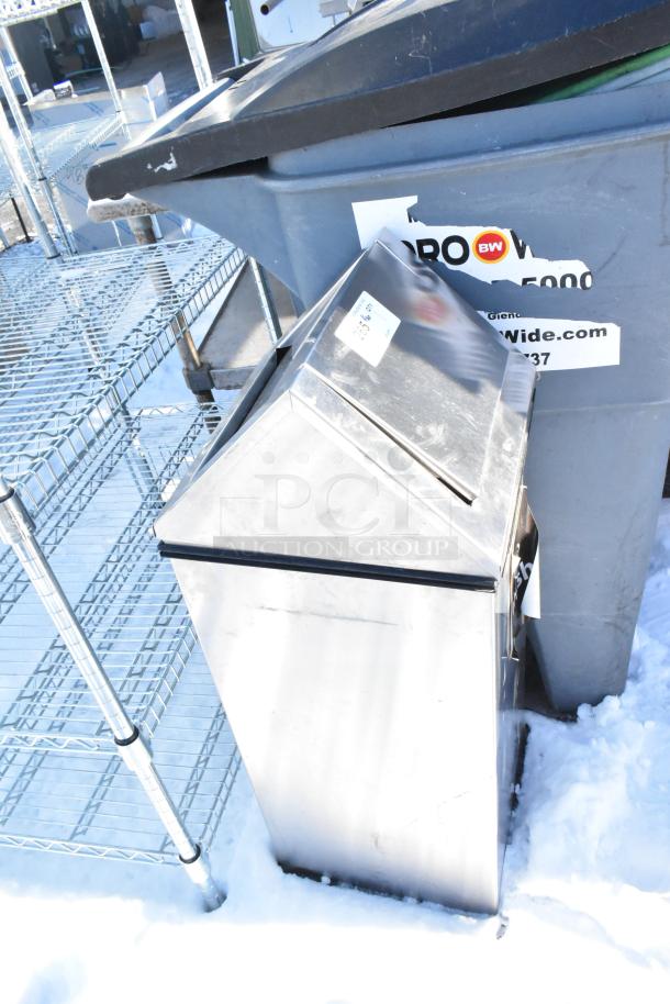 Stainless steel trash can shell in good condition, set on a snowy ground near a larger gray bin with visible labels.