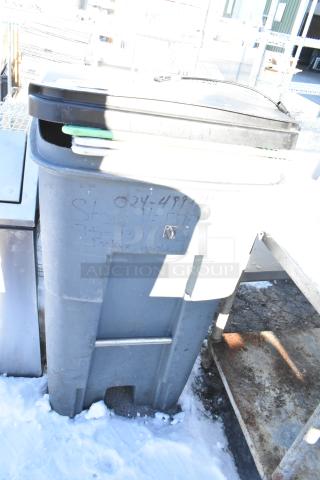 Poly trash can containing multiple cutting boards, visible on top. Exterior shows writing and minor wear, set outdoors.