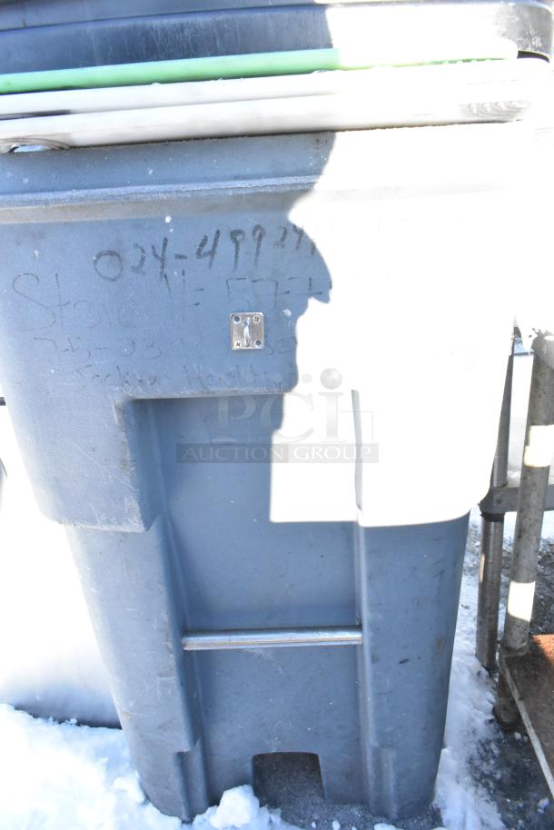 Poly trash can holding cutting boards, visible markings and a latch, moderate wear, outdoor setting with snow.