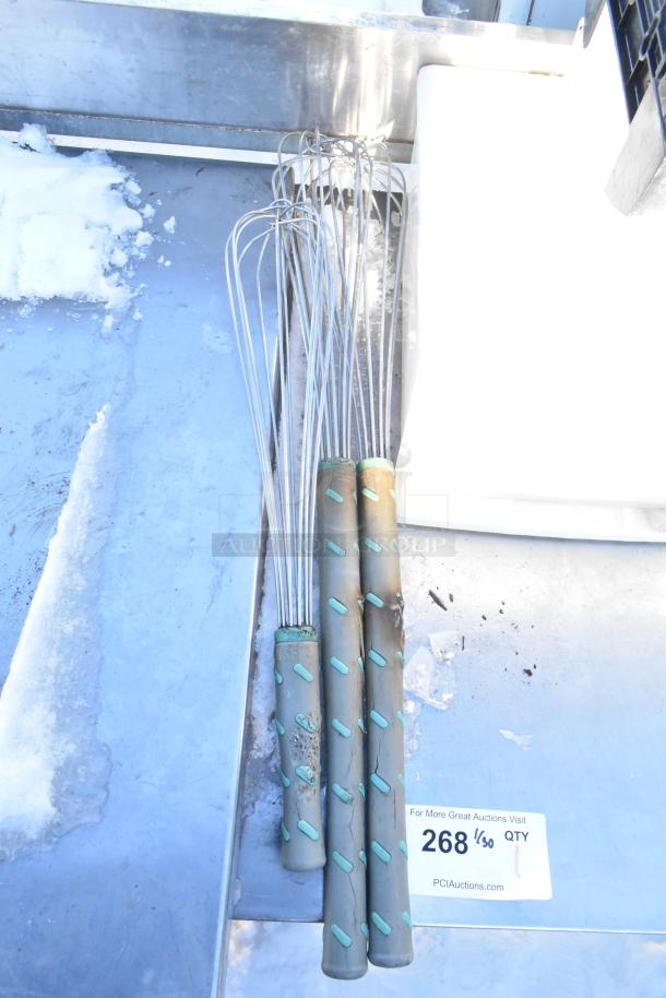 6 kitchen whisks with textured handles on metal surface, worn condition, auction lot label visible.