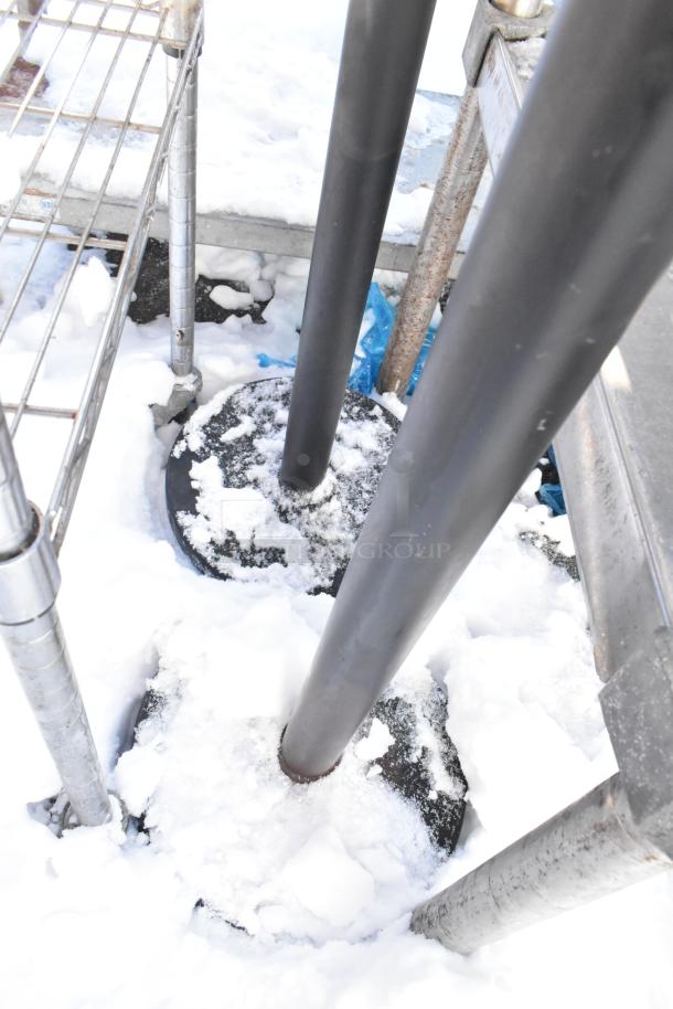 Two Winco CGS-38K stanchions with round bases, partially covered in snow. Ideal for managing queues.