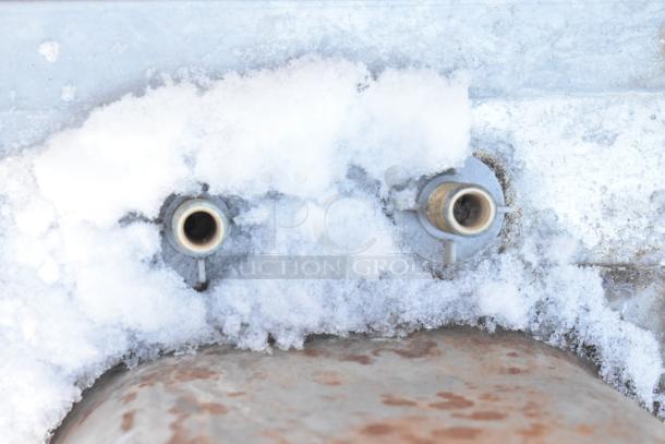 Stainless steel single bay sink, no legs. Snow-covered surface and plumbing fittings visible. No visible brand markings.