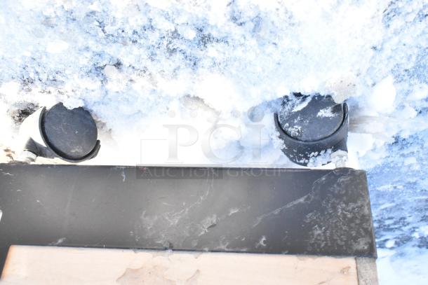 Metal and wood display rack with caster wheels, partially covered in snow, showing signs of wear.