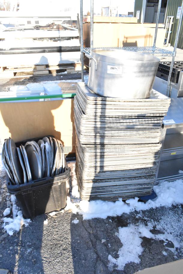 Stack of metal full-size baking pans, metal stock pot, and stock pot lids on display outdoors. 100 times your bid offer.