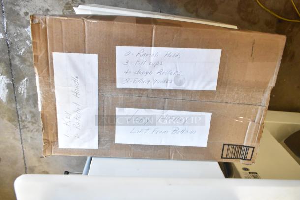 Cardboard box containing Arcobaleno AMF160 Pasta Machine parts, labeled with contents like ravioli molds and filling guides.