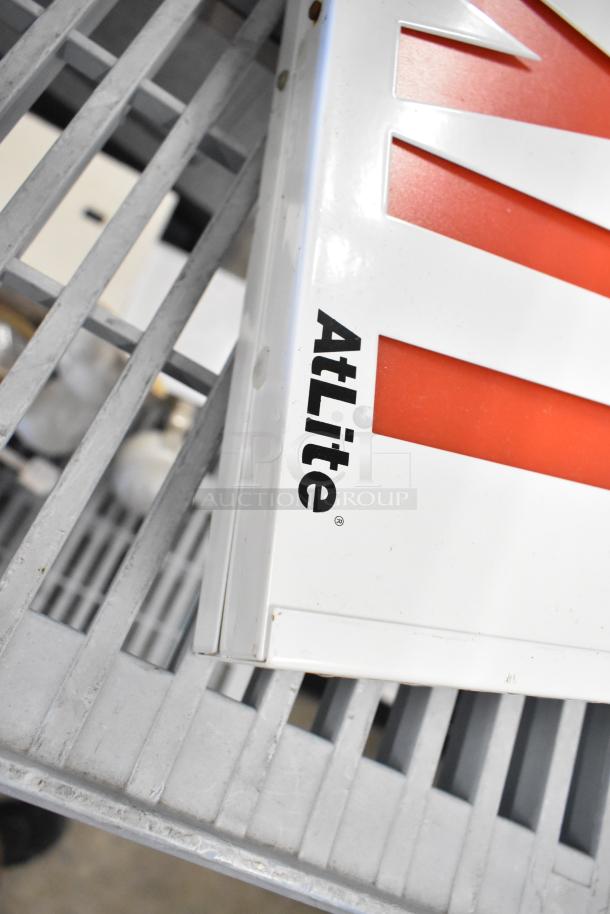 Alt text: AtLite exit sign on metal shelf, part of a lot including emergency lights and Eaton power box. Good condition.