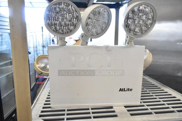 Emergency lights with three adjustable heads, branded AtLite, in good condition. Part of a 19-item auction set.