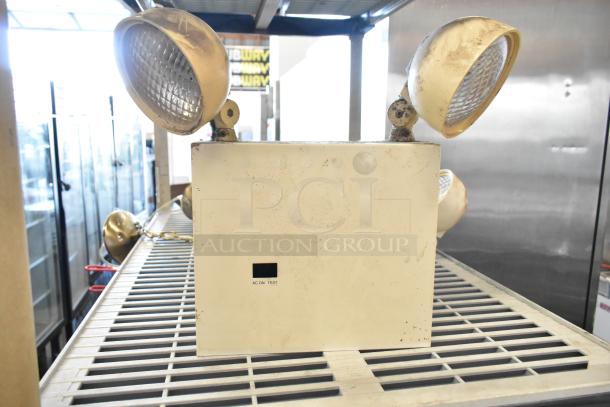Emergency lights with dual lamps and Eaton power box; visible wear; AC ON TEST label. Lot of 19 items.
