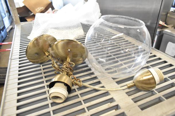 A collection of various electrical items, including a brass fixture and clear glass lamp cover, on a metal grate.