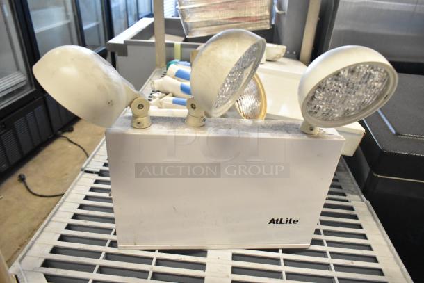 AtLite emergency light with three adjustable heads on a sturdy base, white color, visible dust and mild wear.