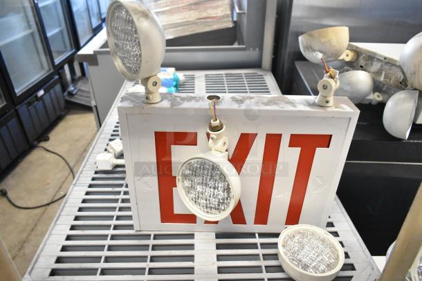 Various items including emergency lights and exit sign on a shelf. Visible wear. Exit sign marked with "EXIT" in red.
