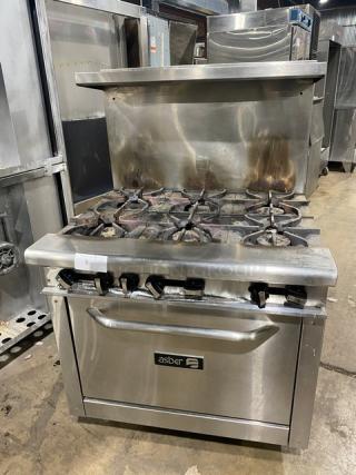 Asber commercial stainless steel 6-burner gas range with oven, backsplash, and salamander shelf. Shows signs of use.