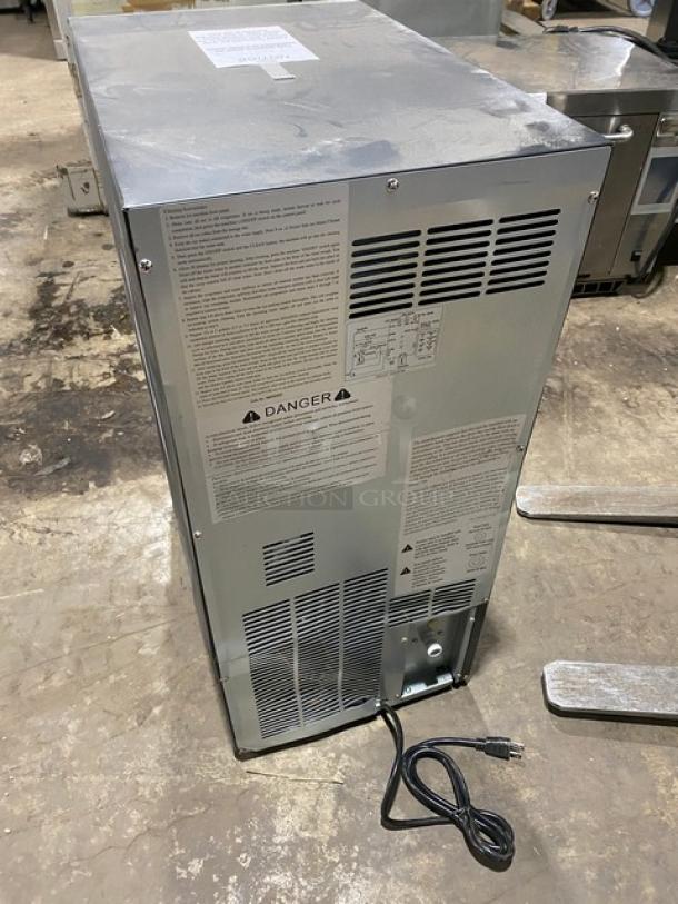 Maxx Ice Model MIM50 stainless steel ice maker seen from the back, showing safety labels and an attached power cord.