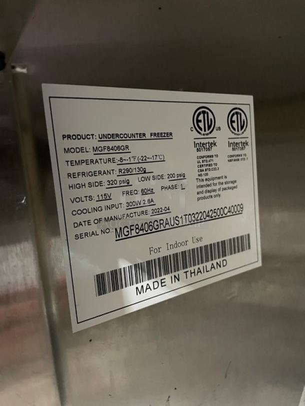 Alt text: Atosa 2022 commercial stainless steel 2-door undercounter 48" worktop freezer, model MGF8406GR, with marble style worktop, up-turned backsplash, and poly-coated wired rack. Serial number MGF8406GRAUS1T0322042500C40009. 115V, 1 phase, on casters. ETL certified label visible. Made in Thailand.