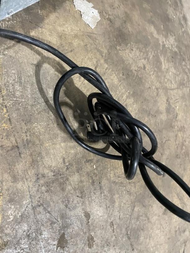 Coiled black electrical cord on a textured concrete floor, part of the Atosa freezer unit.