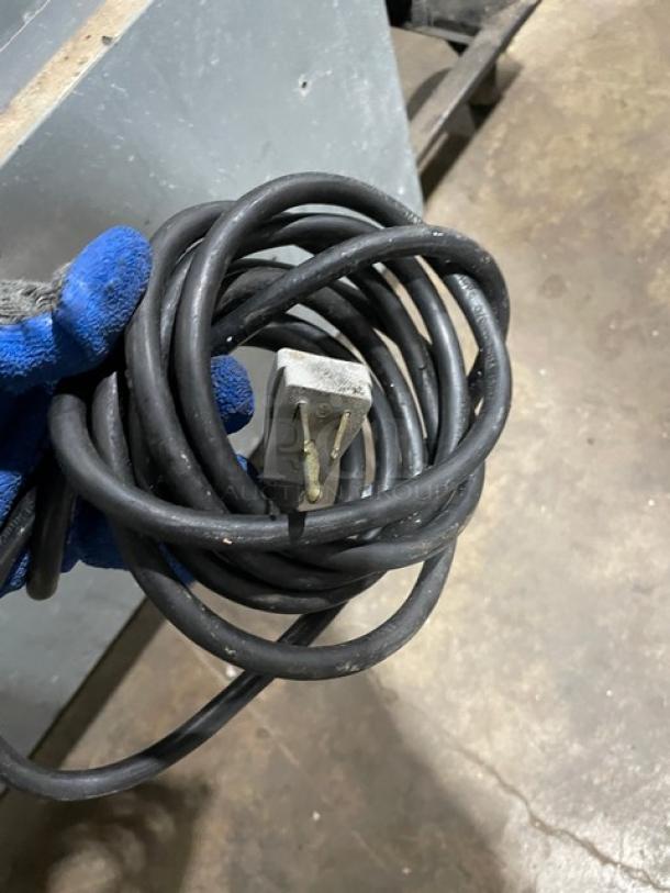 Coiled power cord held by gloved hand, part of True model TUC-48F-D-4-HC undercounter freezer.