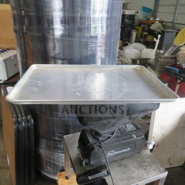 Aluminum 1/2 size sheet pan, visibly used, resting on a black piece of equipment in a workshop setting.