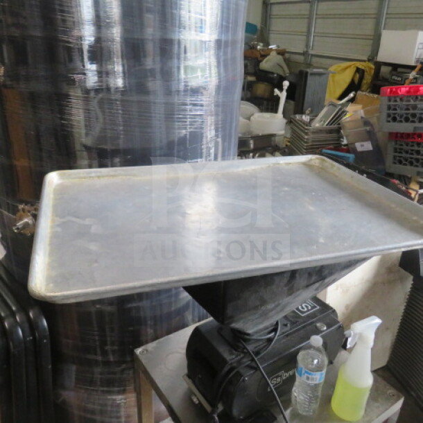 Full-size metal sheet pan, showing slight wear, placed on industrial equipment, surrounded by storage items.