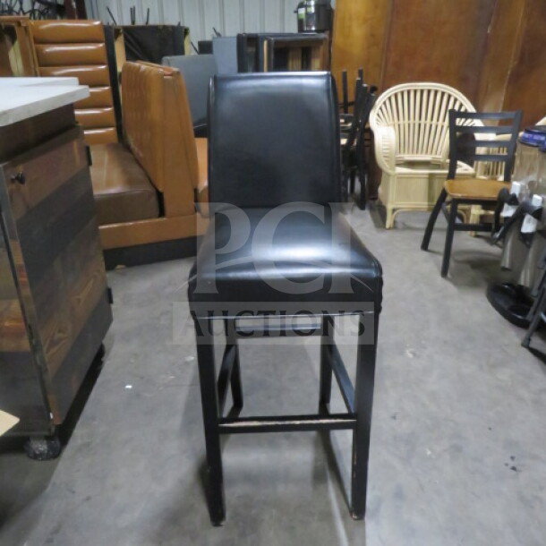 Wooden bar height chair with black cushioned seat and back, footrest; used condition, ideal for bars or kitchens.