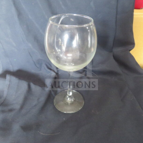 Clear glass stem wine glass on a dark fabric background, showing slight wear. Model: 12XBID.