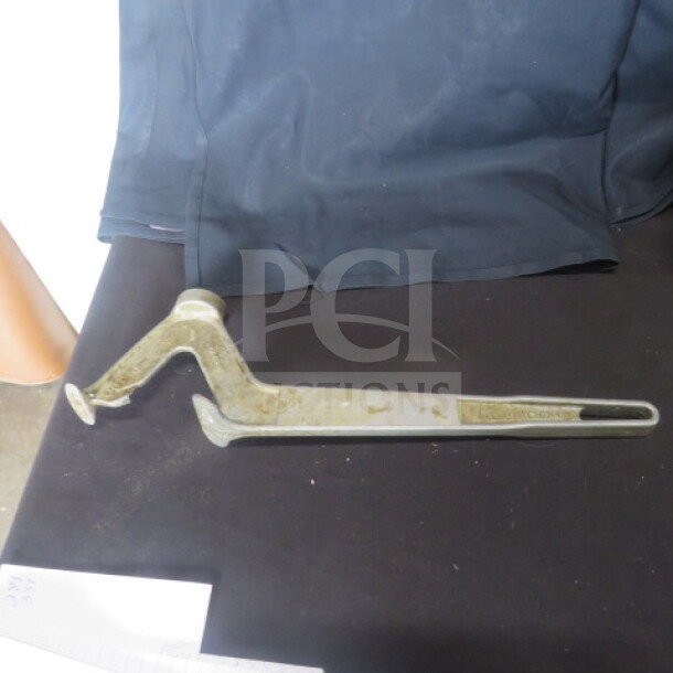 Metal bucket opener with a hooked design, used condition. Appears slightly worn, suitable for opening sealed buckets.