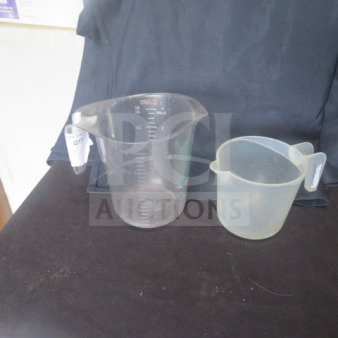 Assorted measuring cups, one large clear plastic with measurements, one smaller translucent. Used, slight wear visible.