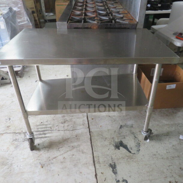 Stainless steel table with undershelf on casters, 48x30x35.5 inches. Durable condition, ideal for kitchen use.