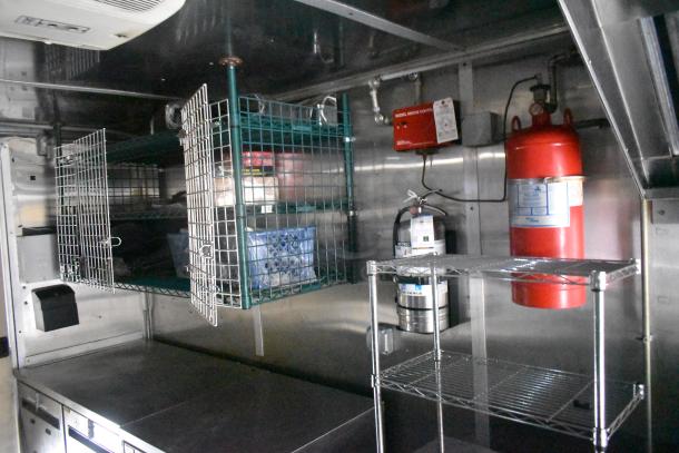 Cruising Kitchens 24' food trailer interior with commercial equipment, wire shelving, fire suppression system, and stainless steel worktops.
