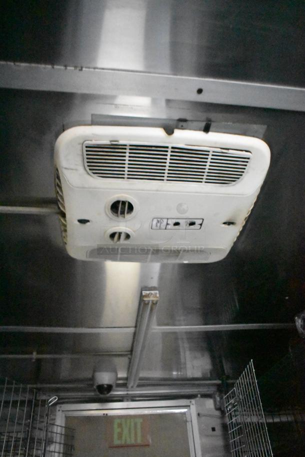 Interior view of a Cruising Kitchens 24' food trailer, showing a ceiling-mounted ventilation unit, metallic walls, and a security camera.
