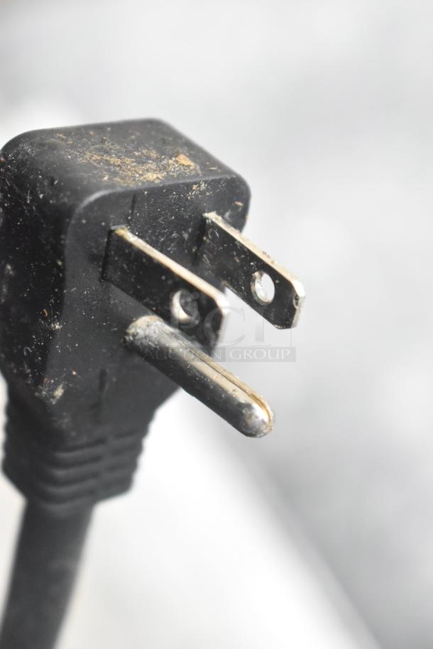 Close-up of a worn three-prong electrical plug on a black cable, dust visible on the surface.