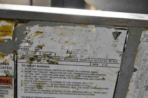 Henny Penny 600 pressure fryer label, showing model and gas specs, stainless steel, on casters; signs of wear.