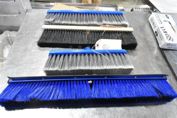 New Lavex push broom heads in various sizes and bristle types displayed on a metal surface, tags attached.