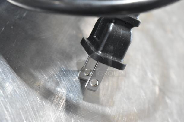 Close-up of Genesis GCS130 circular saw power plug on a metallic surface. New condition with potential scratches or dents.