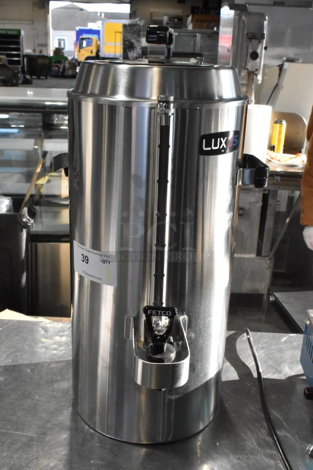 Brand new Fetco TPD-30 Luxus 3-gallon stainless steel coffee dispenser, minor scratches, visible "LUXUS" and "FETCO" markings.