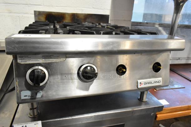 Garland stainless steel commercial gas-powered 4 burner range, featuring control knobs, used condition, visible branding.