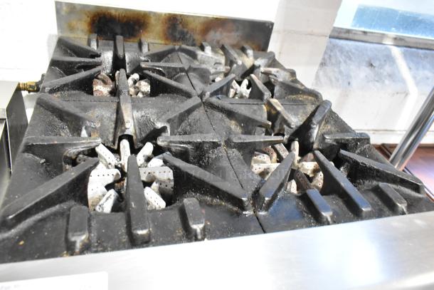 Garland stainless steel commercial 4-burner gas range, showing minor wear. Durable cast iron grates, ideal for heavy use.