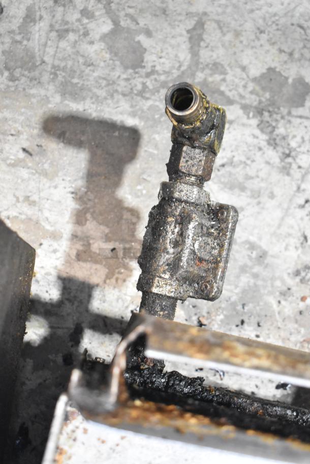 A gas connection on a stainless steel commercial countertop gas-powered flat top griddle, showing signs of wear.