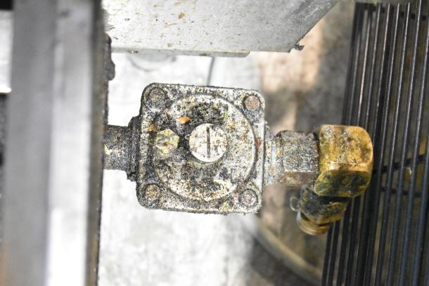 Garland stainless steel commercial 4-burner gas range seen from underside, showing gas connection, appears used and worn.