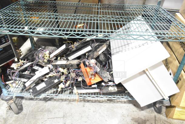 Lot of various ballasts on a metal shelf. Includes mixed models, visible wiring, and some labels. Marks indicate used condition.