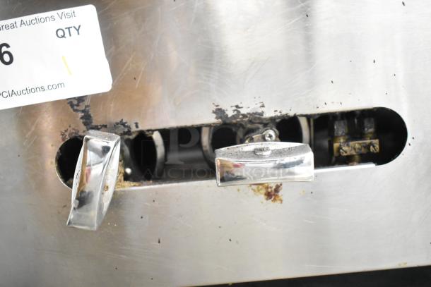 Stainless steel commercial single burner stock pot range, gas powered, showing wear and oxidation around control knobs.