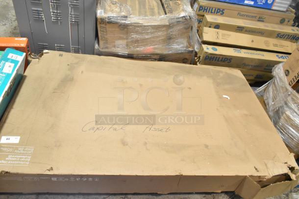 Original box of Samsung QM85C 85" LED Display TV on warehouse floor. Box appears slightly worn. Local pickup required.