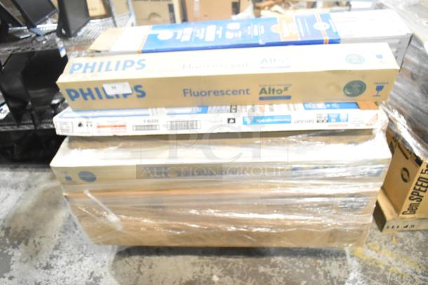 Stack of new lighting items including Philips Fluorescent, GE T8 LED, and Sylvania tube lights, boxed and shrink-wrapped.
