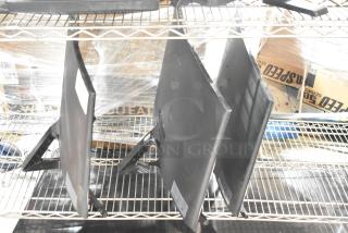 Three computer monitors, including Samsung C27F396FHN, on metal shelving in used condition, with visible mounting brackets.