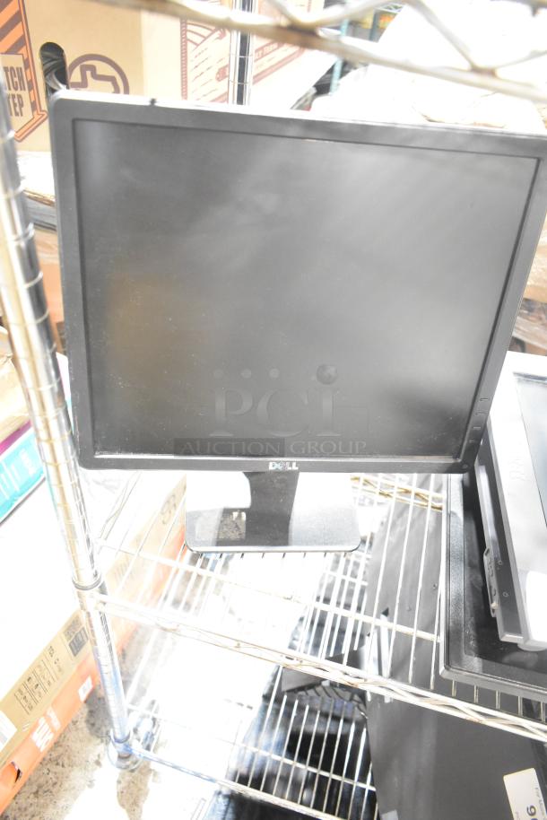 Five computer monitors on a metal shelf, including a Dell monitor. Appears in used condition. No visible markings.
