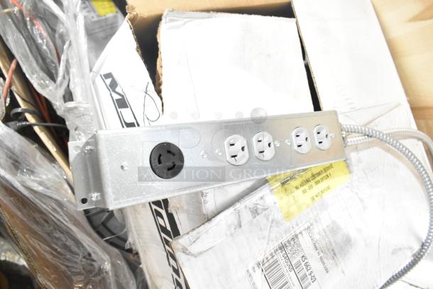 Metal power distribution unit with three outlets and a round connector, mounted on a cardboard box. Items include cables and monitor.